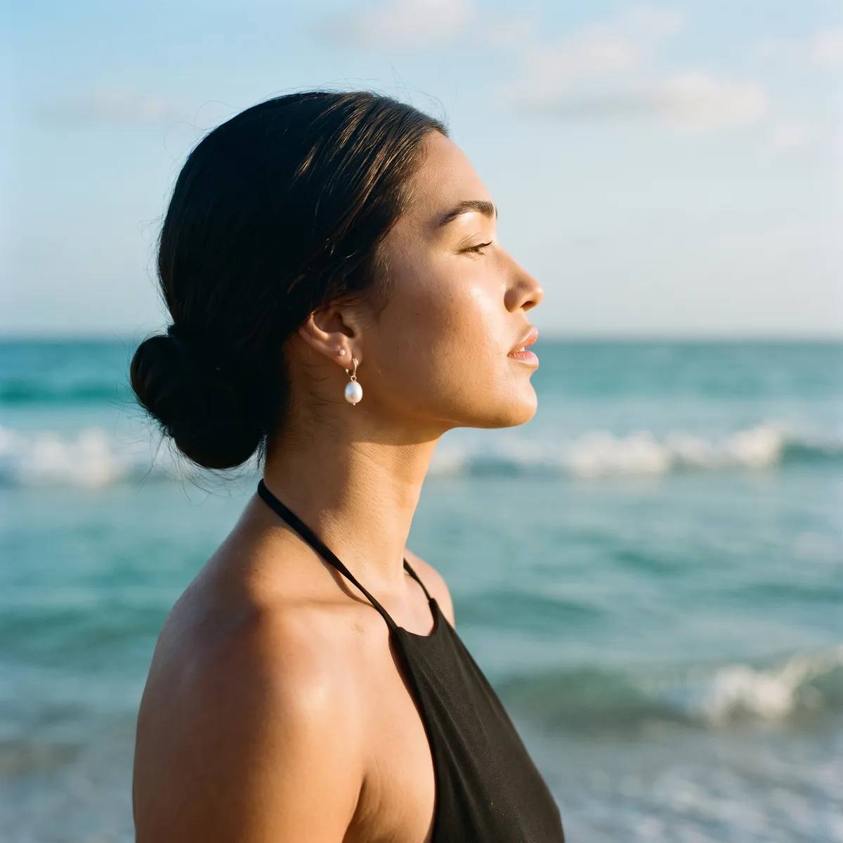A woman in profile with her chin slightly lifted and a clean, defined jawline, the sea behind her