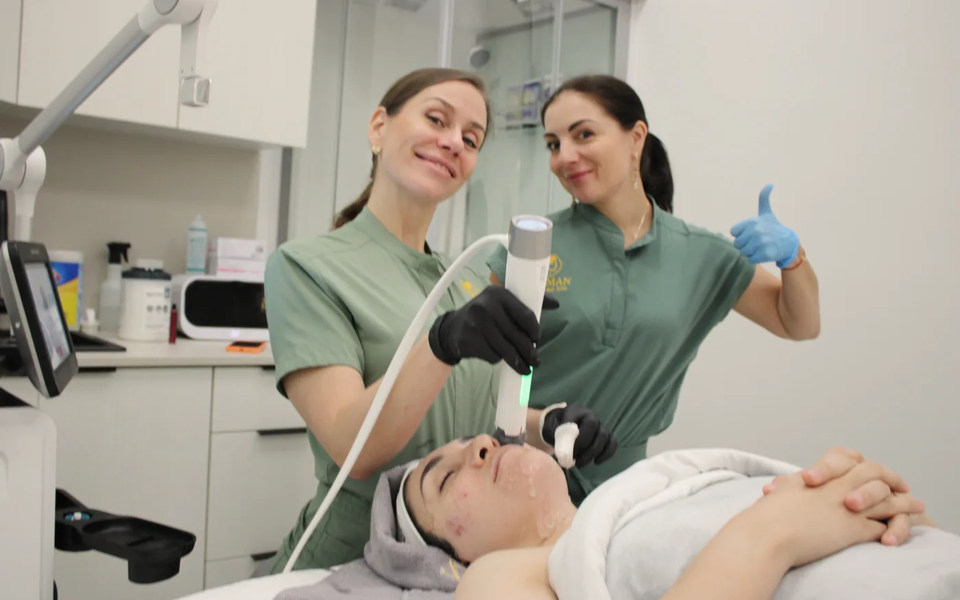 Two WO/MAN specialists smiling during a facial treatment, one giving a thumbs up
